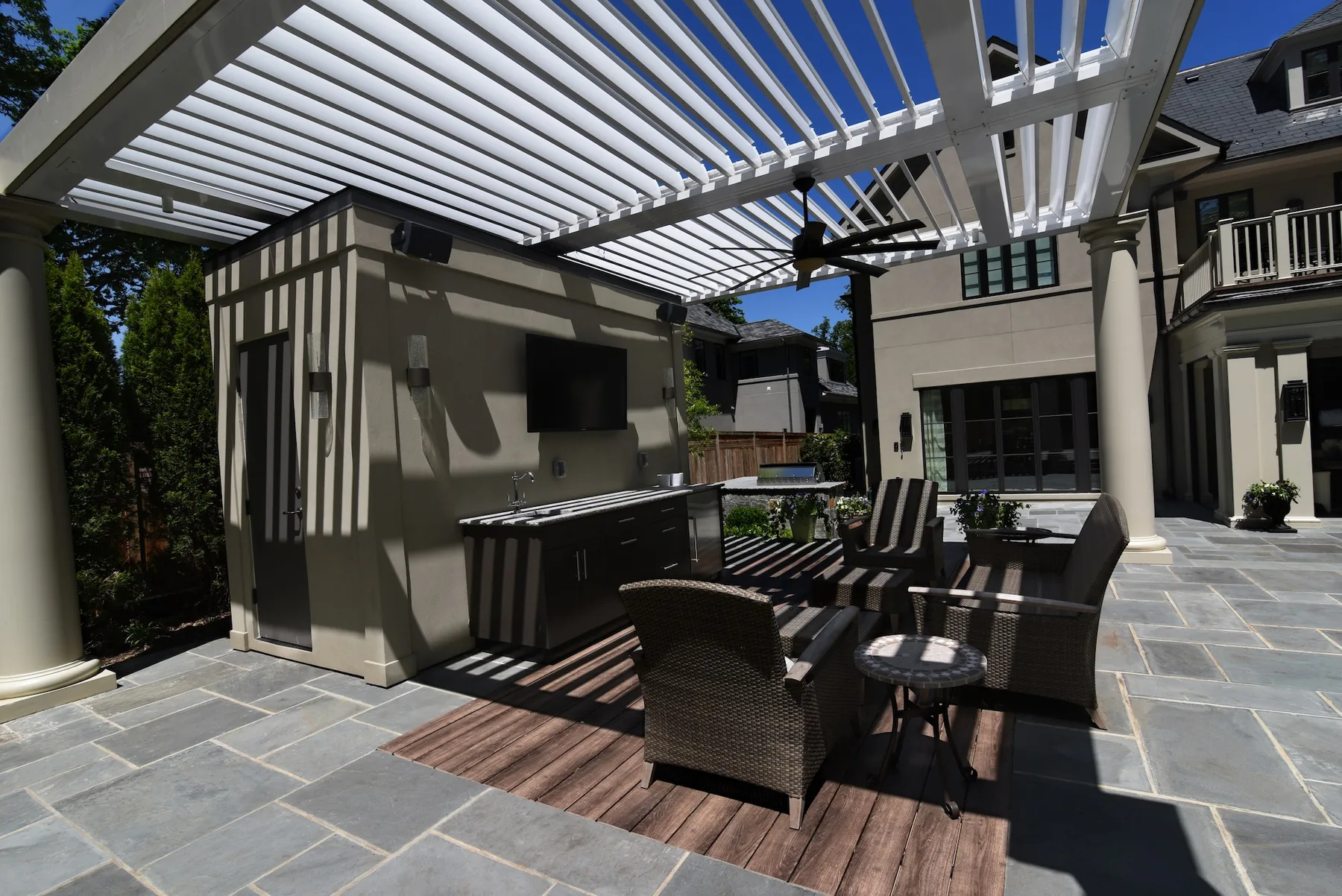 Dining table beneath a white pergola beside the house.