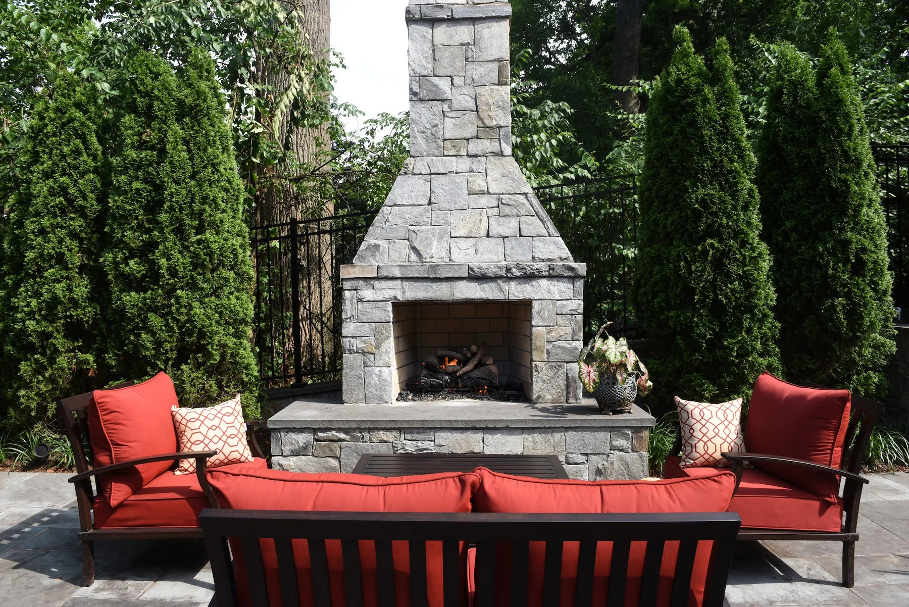 Stone fireplace with red-cushioned seating and evergreen planting.