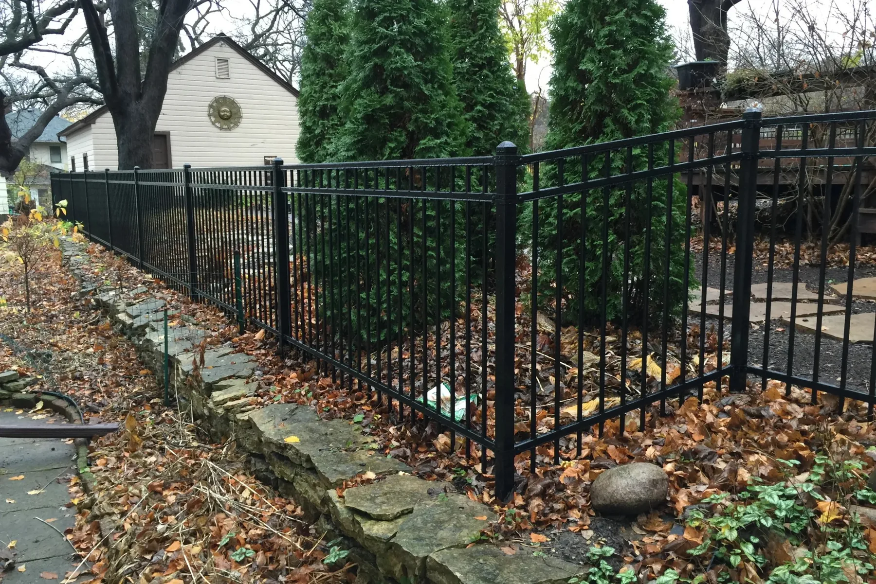 Open metal fencing beside stone edging and mature trees.