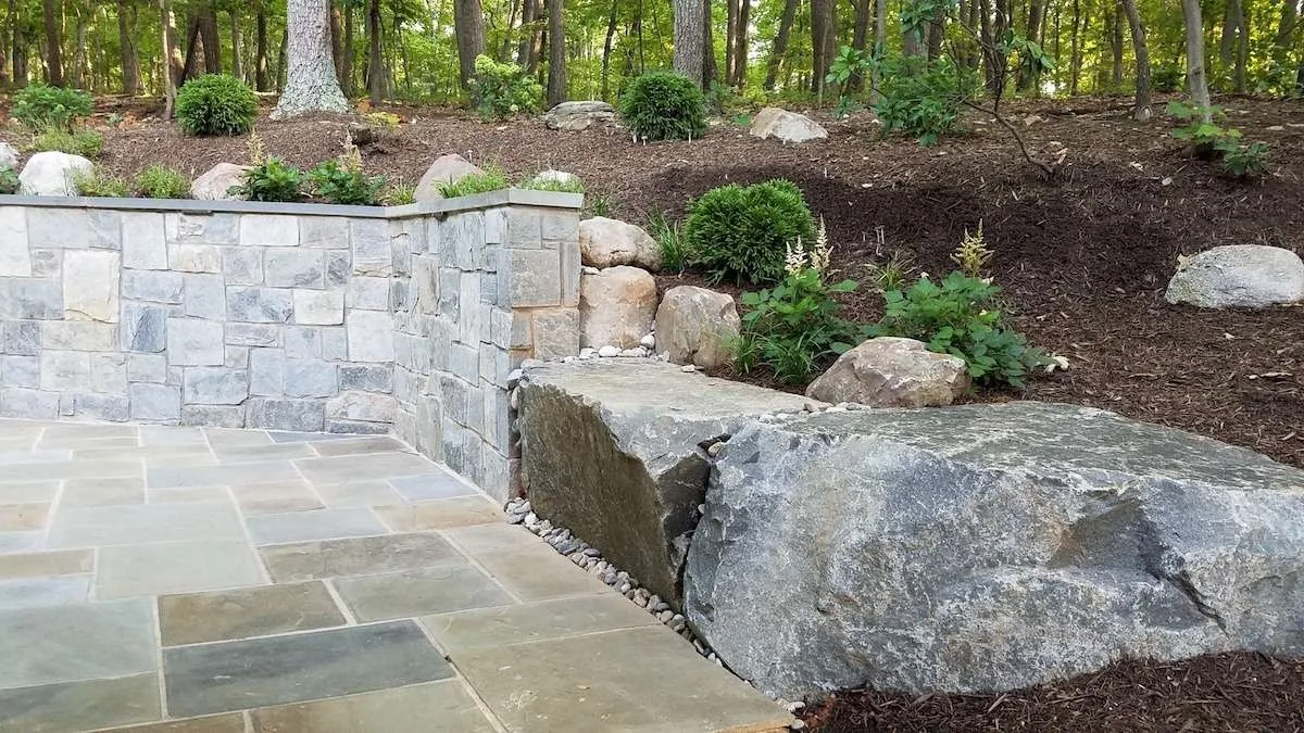 Boulders meeting a stone retaining wall and planted bank.
