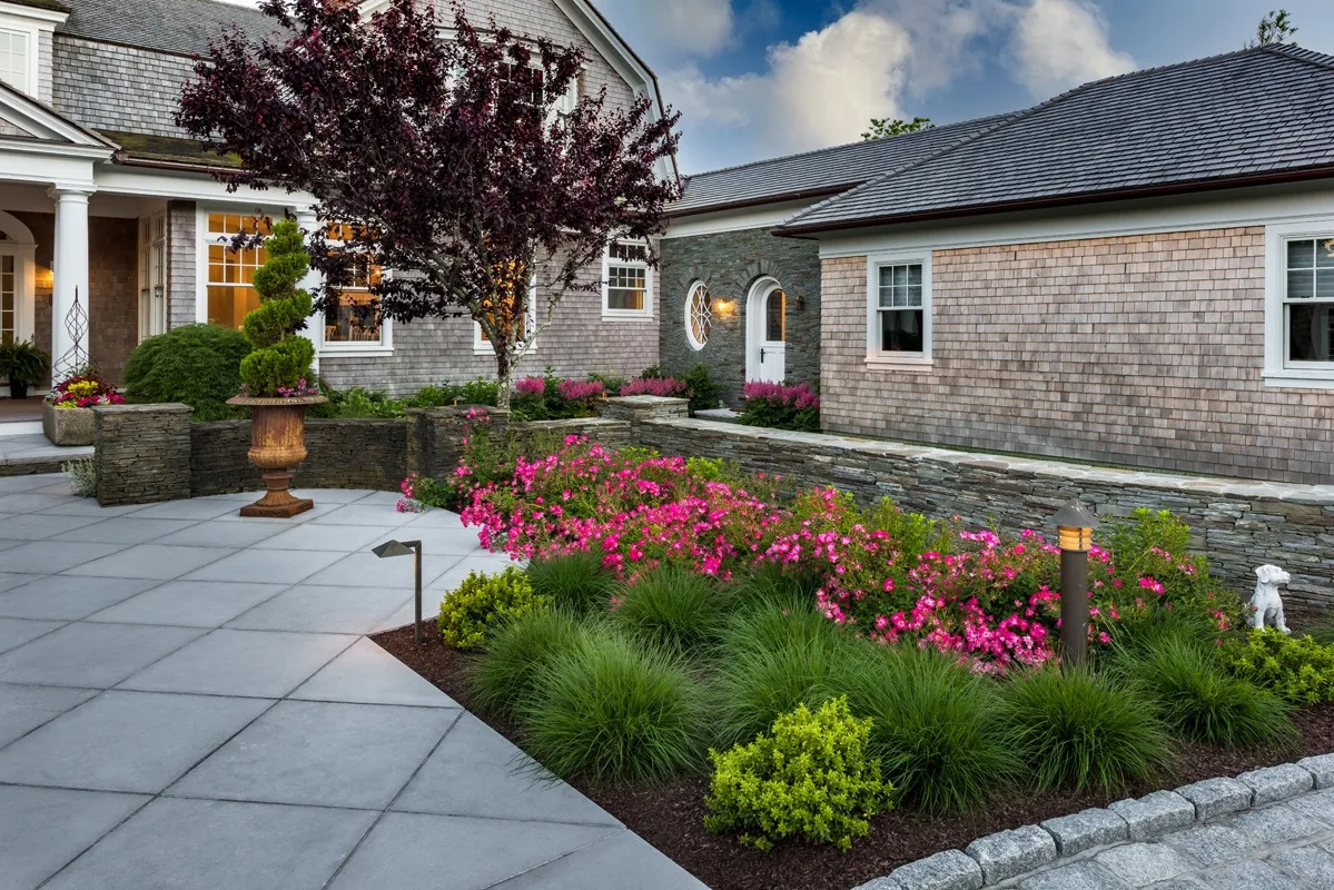 Limestone arrival court beside fieldstone walls and flowers.