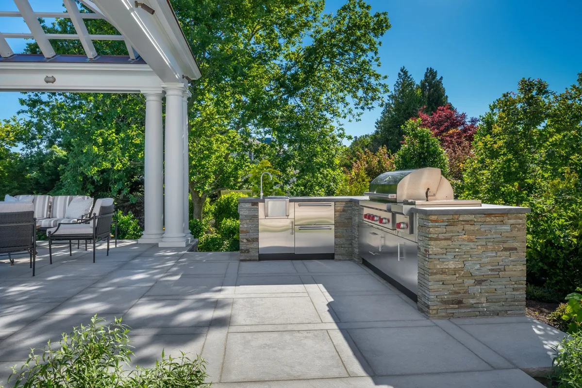 Outdoor kitchen with stone counters under a pergola.