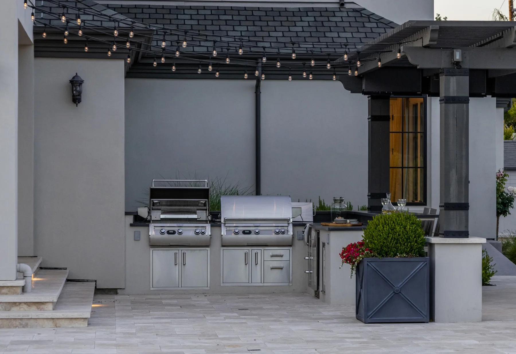 Two grills beneath a pergola beside the house.