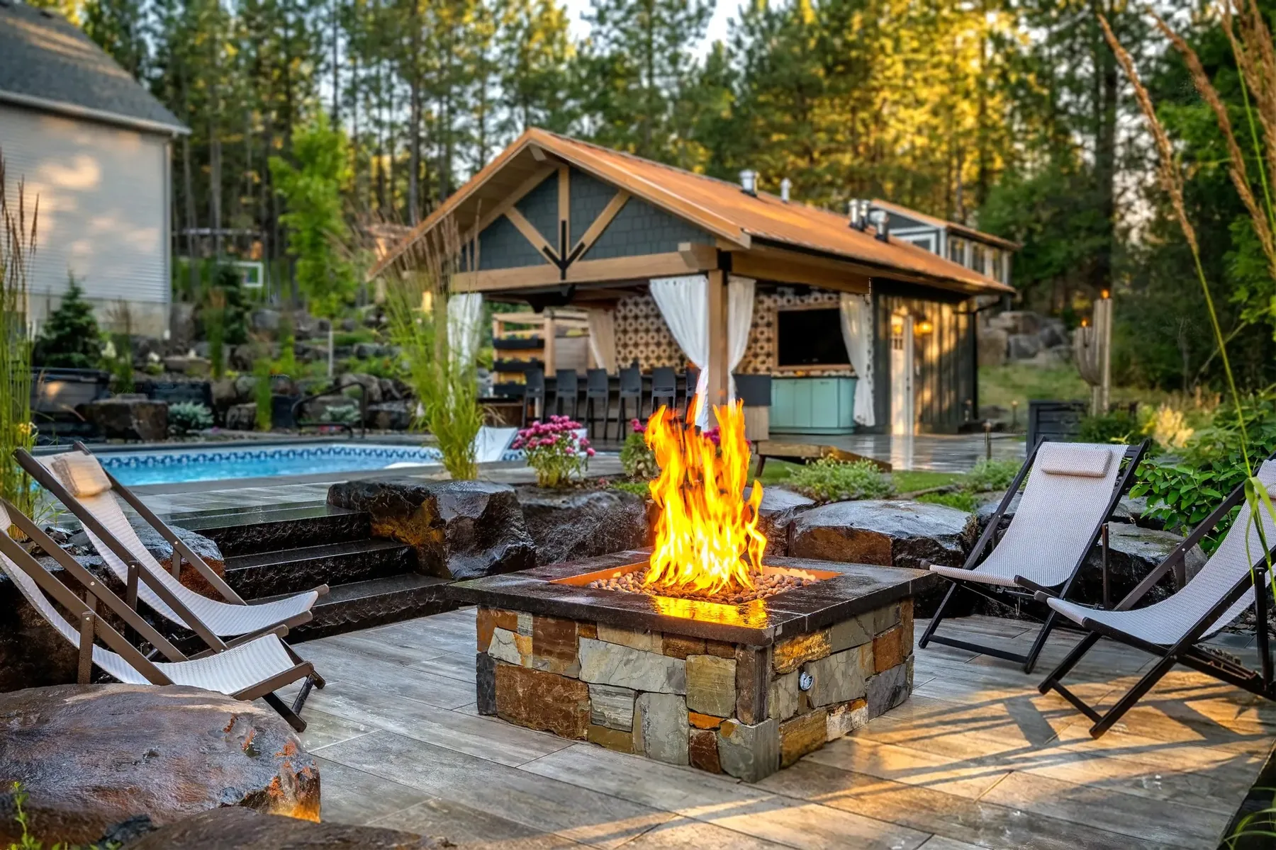 Fire pit with chairs and boulder seating below the pool.