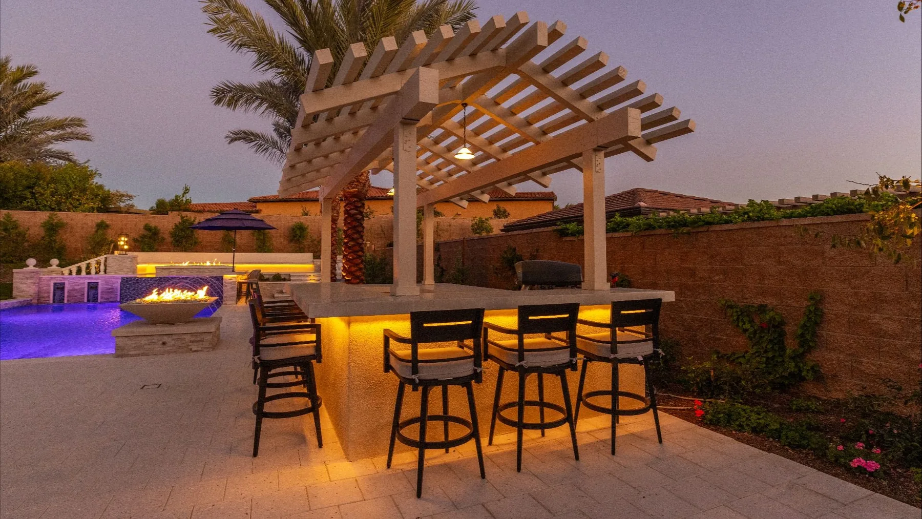 Outdoor bar beneath a timber pergola at dusk.