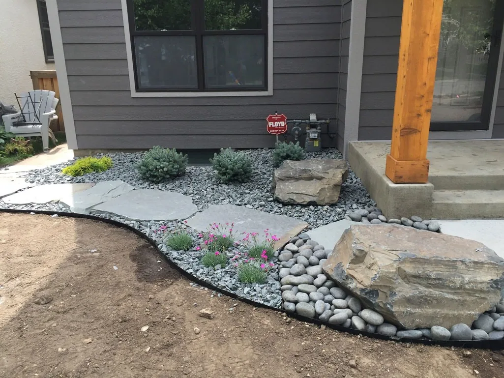 Flagstone path through a gravel bed beside a gray house.