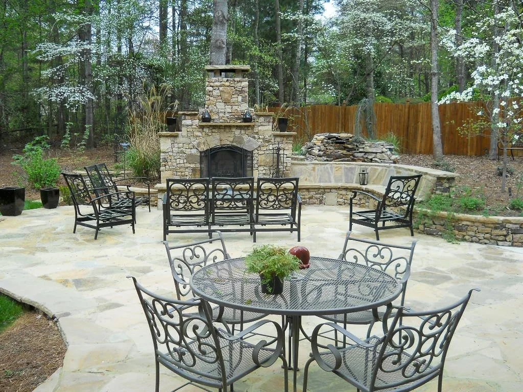 Dining table and chairs facing a stone outdoor fireplace.
