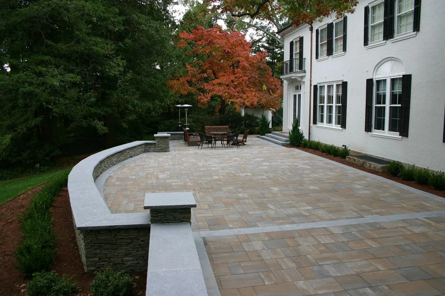 Curving patio beside a white house with dark shutters.