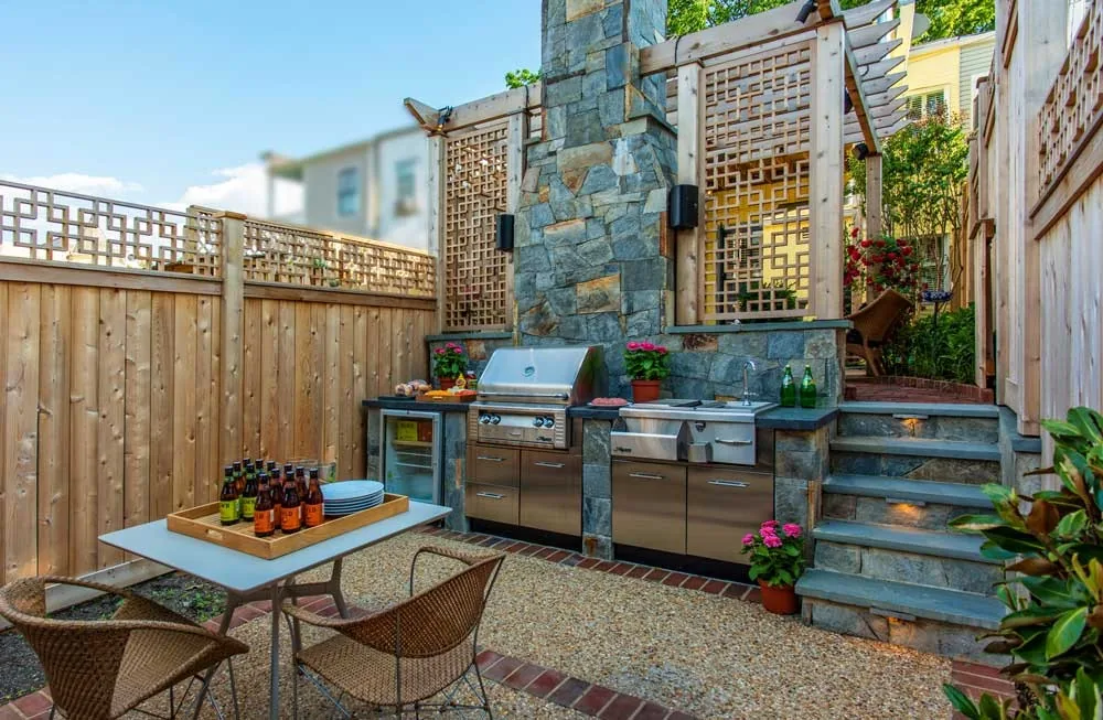 Compact courtyard with masonry kitchen, dining table and steps beside a brick home.