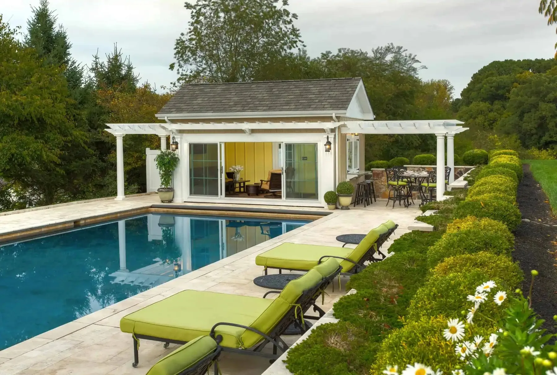 Pool house and green loungers beside an existing pool.