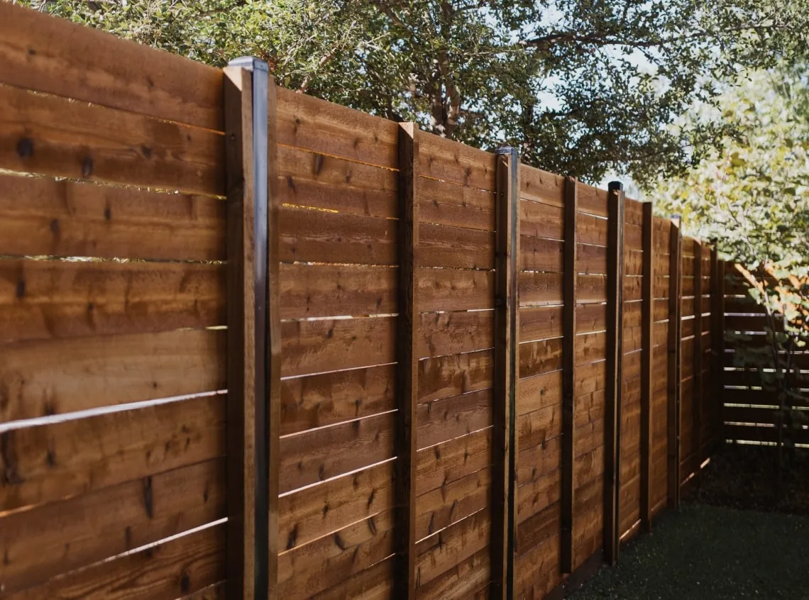 Horizontal wood fence with dark metal posts beside a narrow yard.