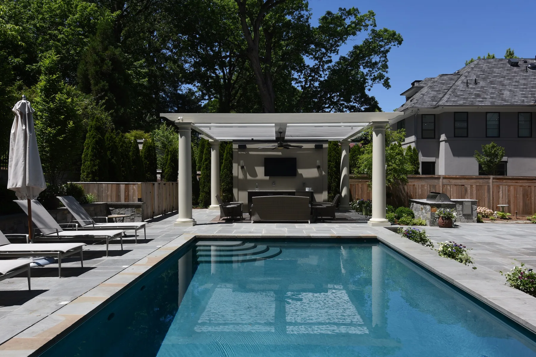 Rectangular pool facing a pale pergola and outdoor kitchen.