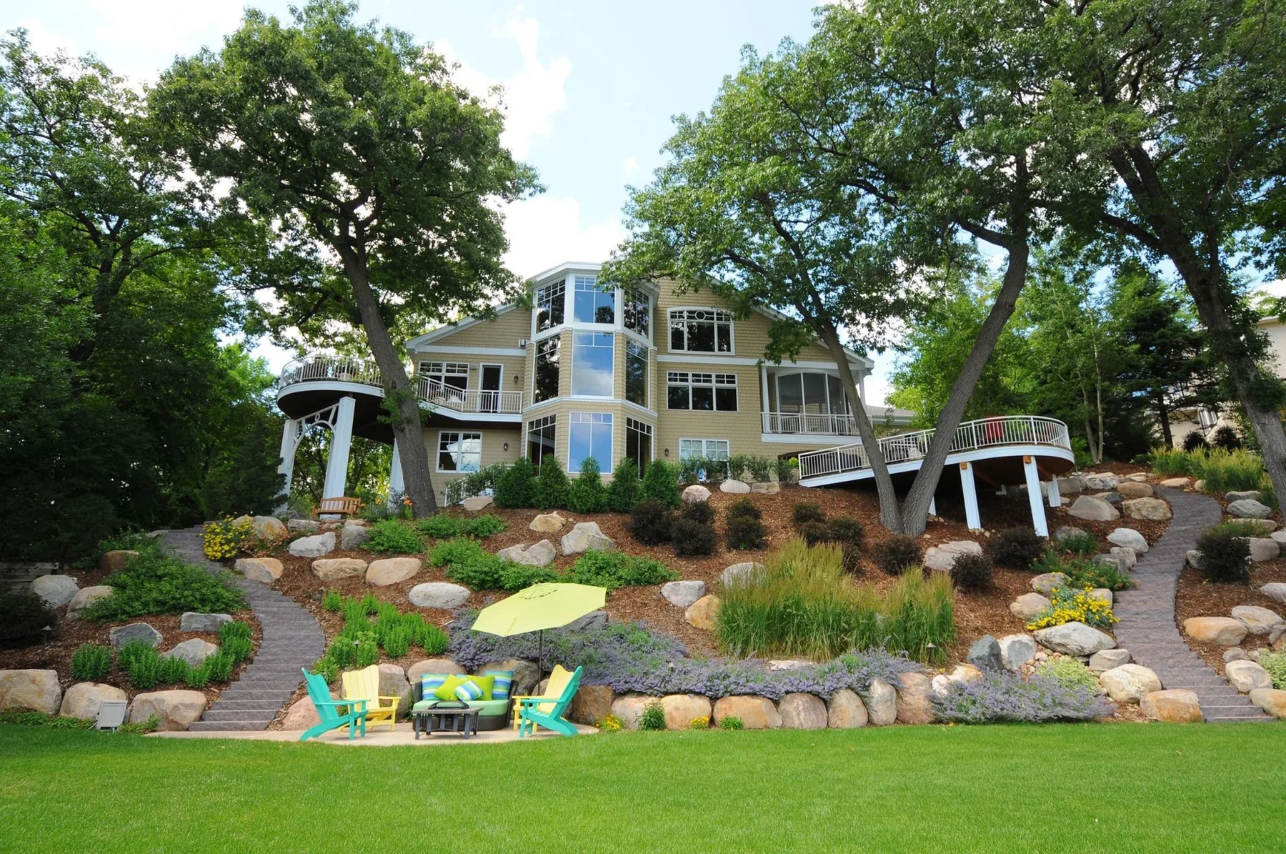 House above terraced planting, boulders and a lower sitting area.