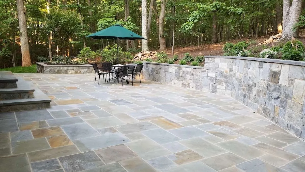 Flagstone patio and retaining wall below a wooded slope.