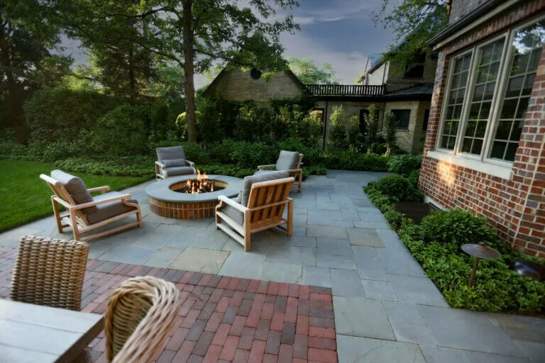 Bluestone terrace with fire pit beside a brick home.