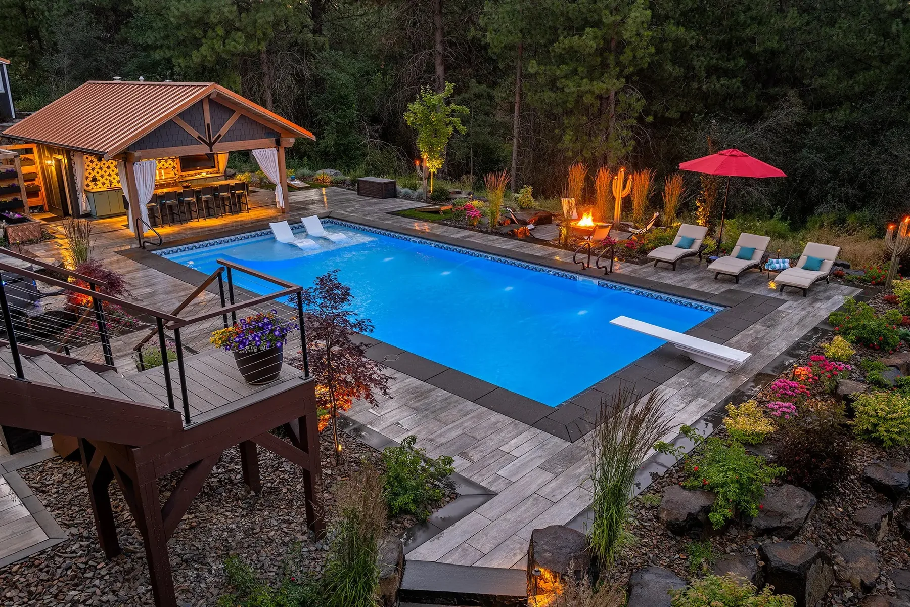 Pool, cabana and sunken fire area on a wooded hillside.