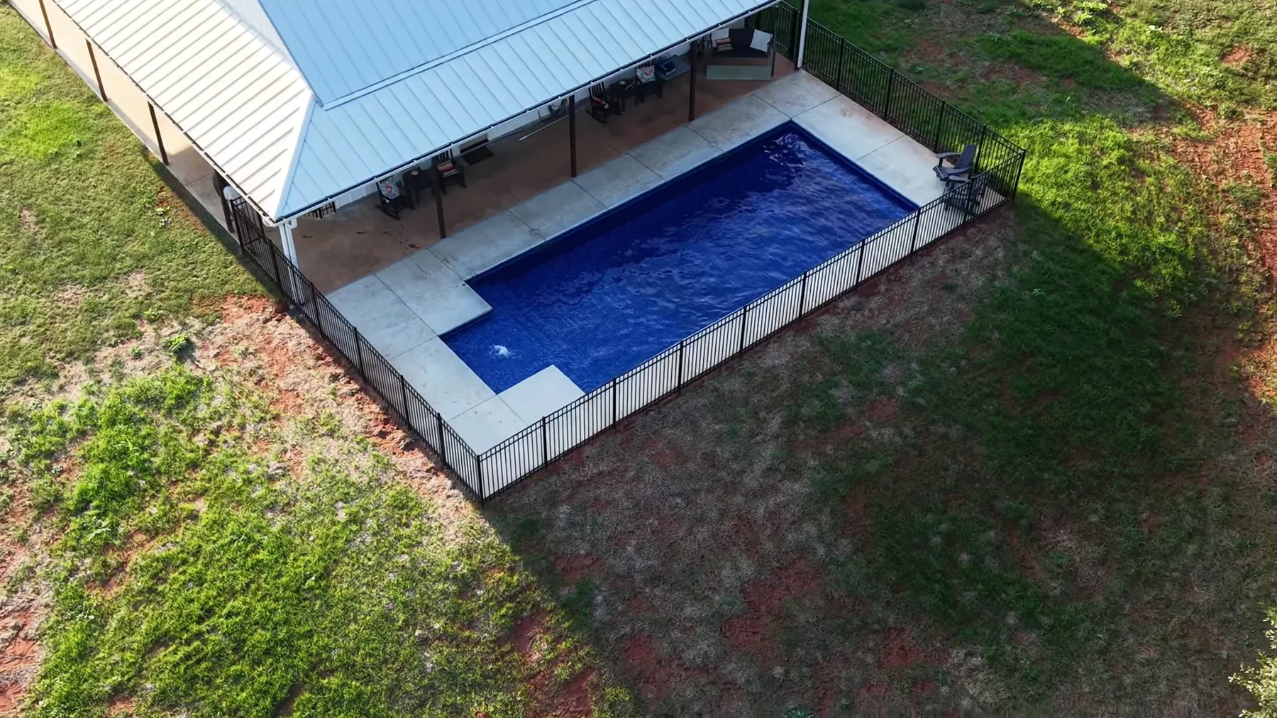 Rectangular swimming pool beside a long covered building.