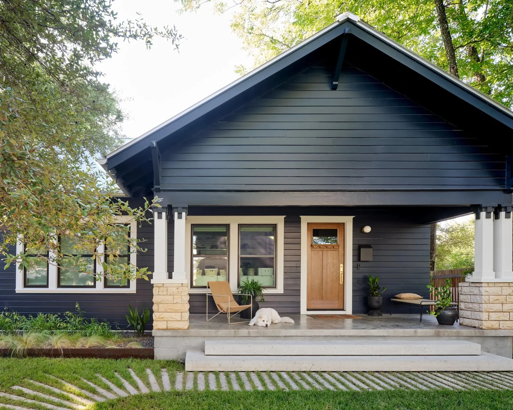 Dark-painted bungalow behind a lawn and timber fence.