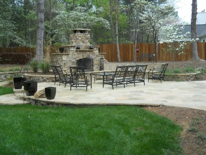 Stone fireplace and furnished terrace at the edge of a lawn.